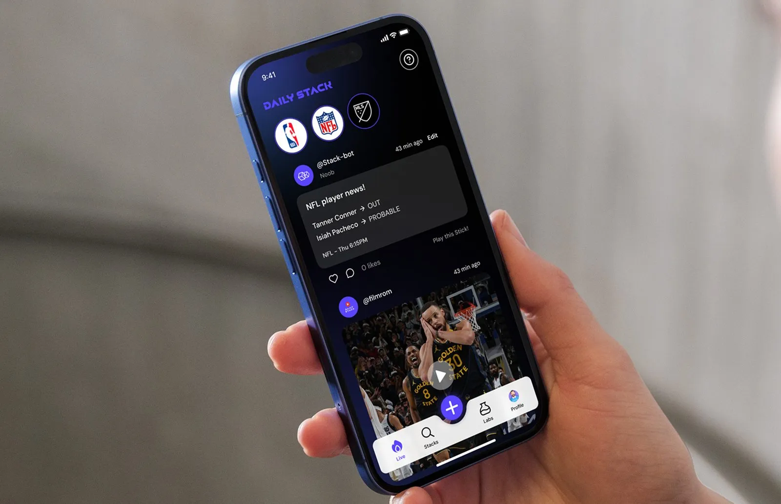 A hand holding a phone at an angle, showing the Daily Stack home feed with NBA, NFL and MLS badges, an NFL player news post and a video post below.