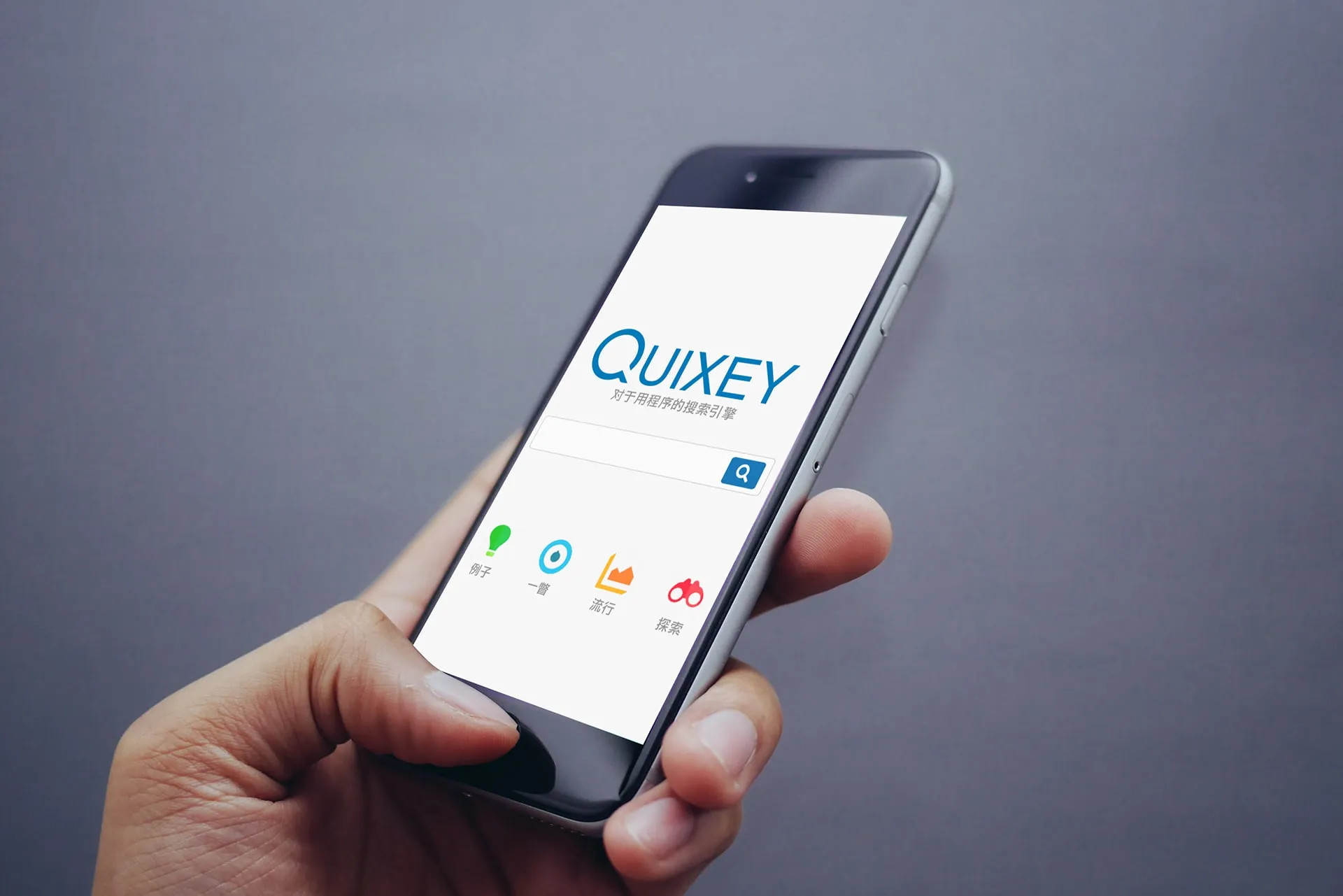 A hand holding a phone showing the Quixey home screen, with the logo, a search field and four icons labeled in Chinese.