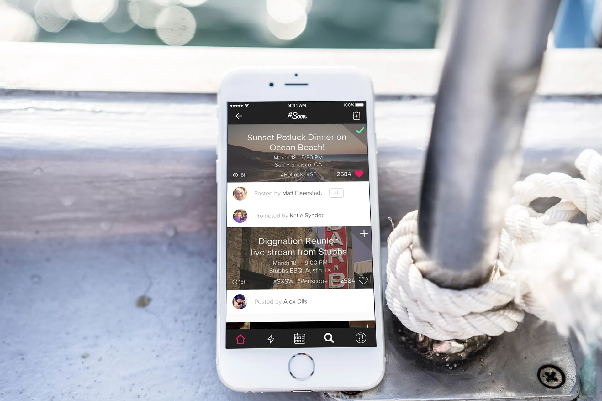 A phone propped against a boat fixture showing the Soon home feed in a dark theme, with two event cards, poster names, a heart count and a tab bar.